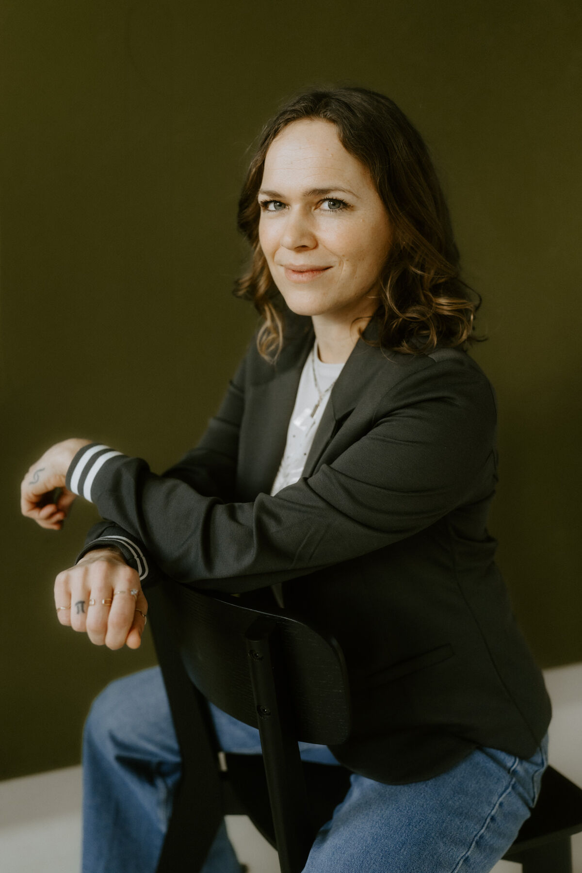 Raphaela Grollius sitzt auf einem Stuhl vor einer olivgrünen Wand