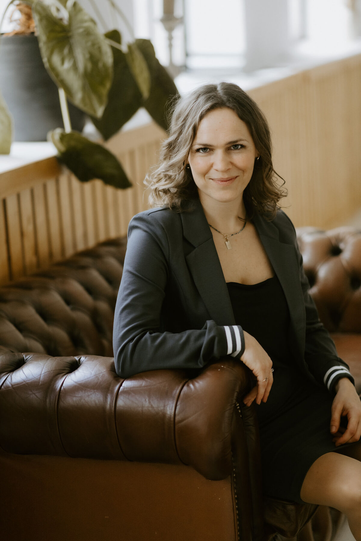 Raphaela Grollius sitzt lächelnd auf einem braunen Chesterfield-Sofa